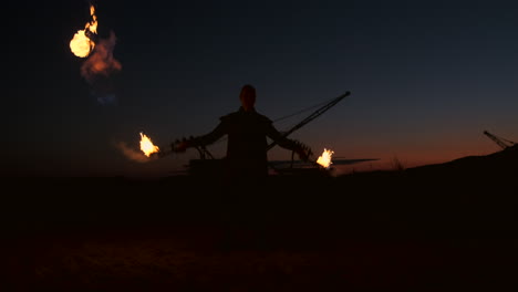 A-man-in-a-raincoat-with-two-flamethrowers-lets-out-a-fiery-flame-standing-at-sunset-on-the-sand